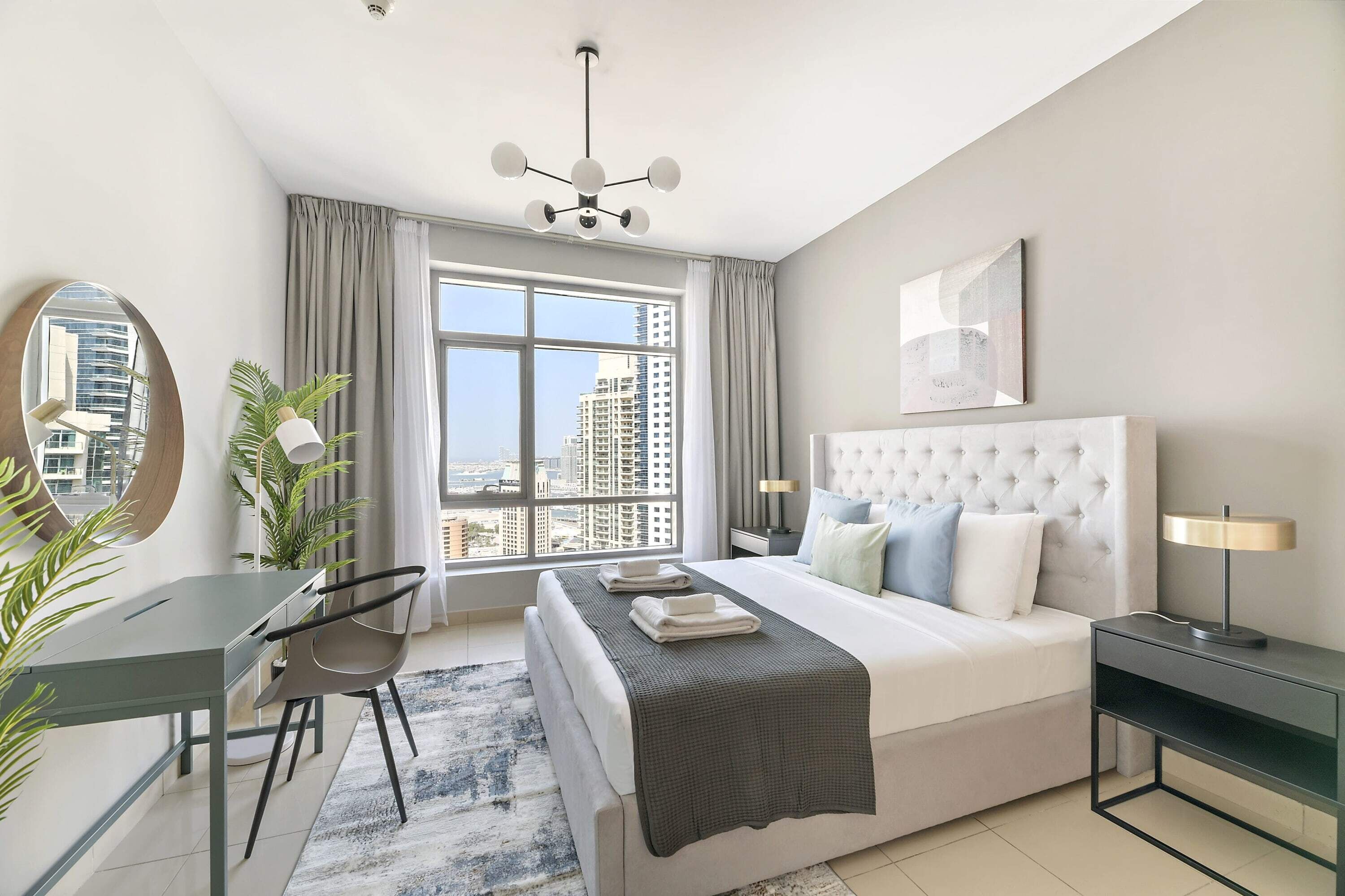 A modern hotel room with a large bed, a desk, and a view of the city.