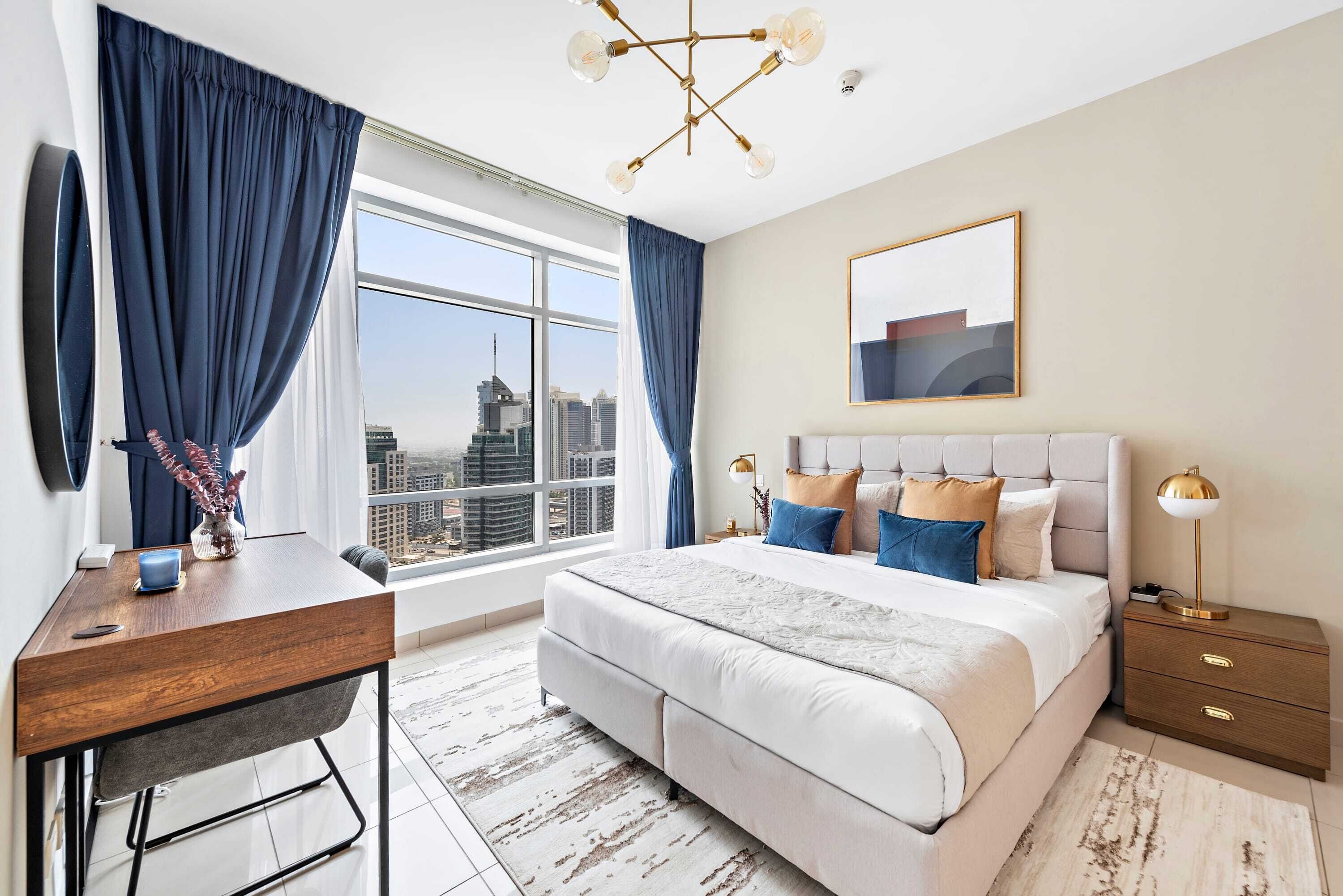 A modern bedroom with a large bed, a desk, and a view of the city.
