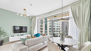 A modern living room with a sofa, dining table, chairs, a TV, and a large window with a city view.