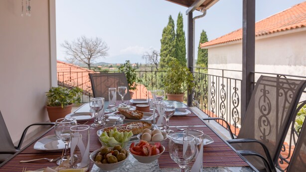 A table set for a meal with various dishes and drinks, overlooking a scenic view with buildings and trees.