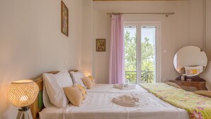 A hotel room with two beds, a bedside lamp, a window with curtains, a mirror, and a view of greenery outside.