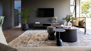 Un salon moderne avec un téléviseur à écran plat, une grande plante en pot, une table basse ronde et un canapé.