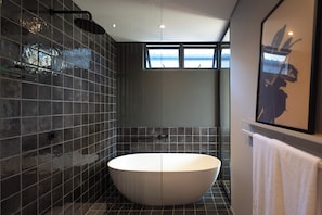 A modern bathroom with a freestanding bathtub, tiled walls, a shower area, and a window providing natural light.