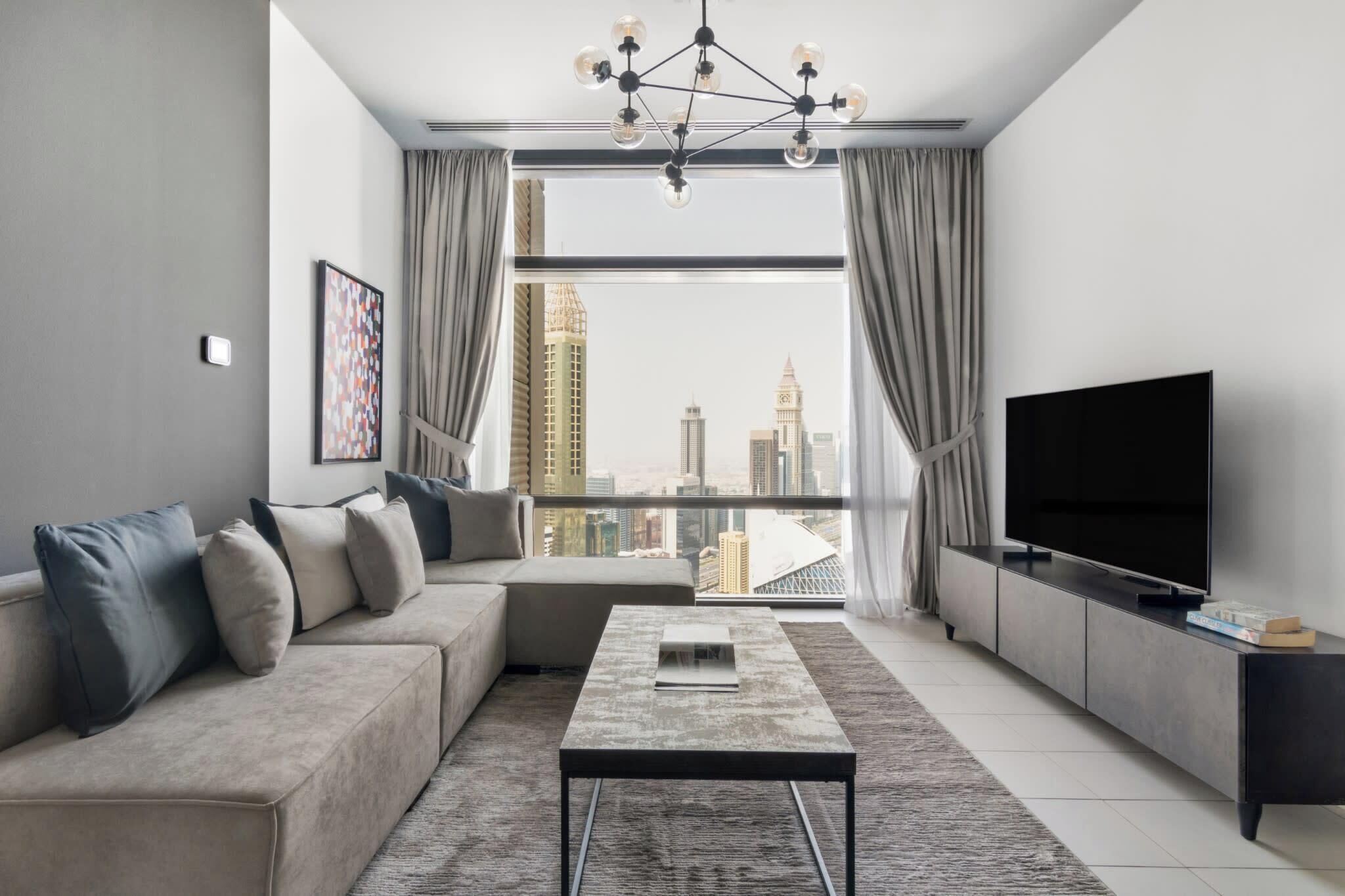 A modern living room with a sofa, a coffee table, a TV, and a view of a cityscape through large windows.
