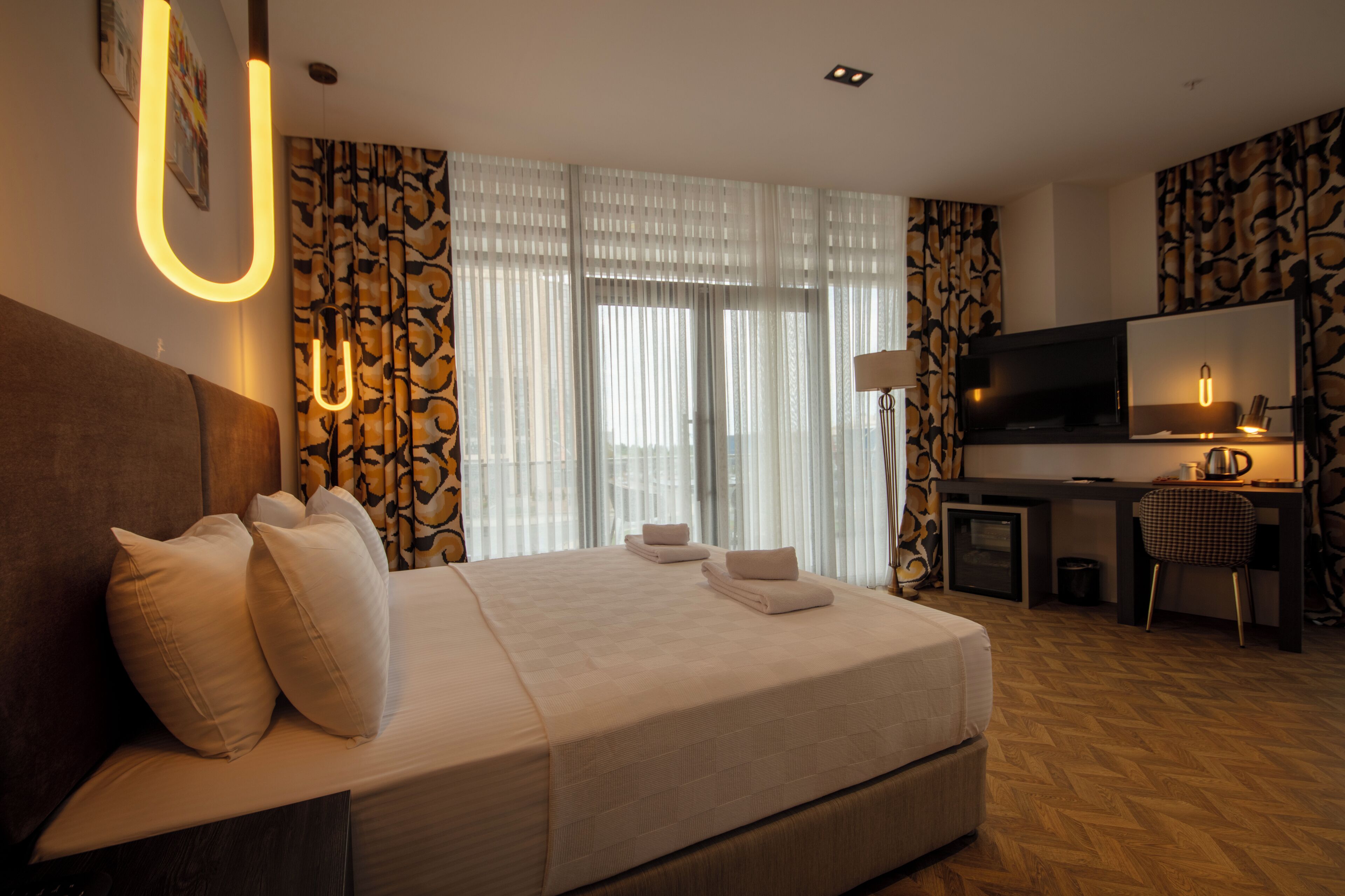 A hotel room with a large bed, a desk, a television, and a window with curtains.
