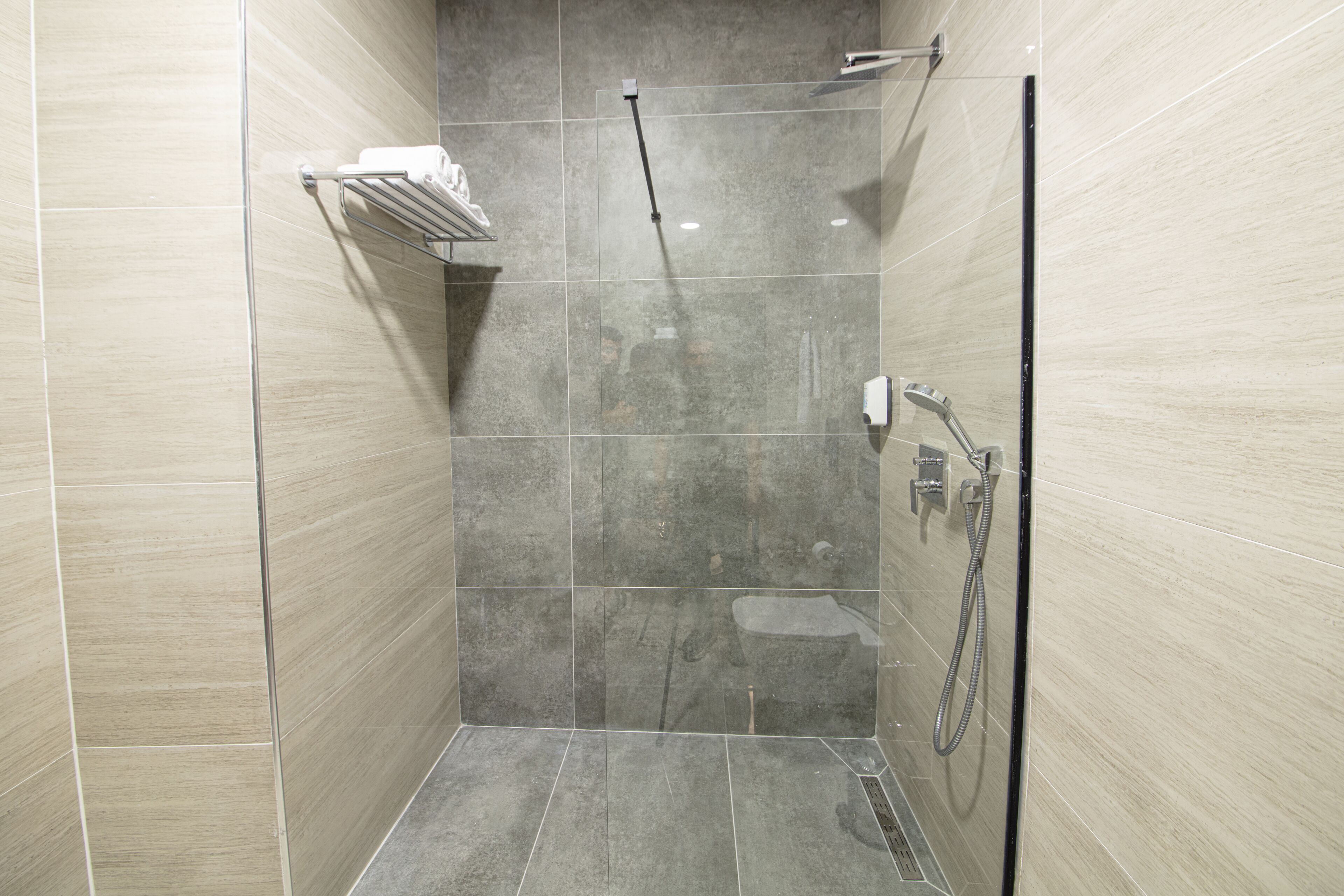 Un área de ducha moderna con puerta de vidrio, un cabezal de ducha de mano y un perchero para toallas.