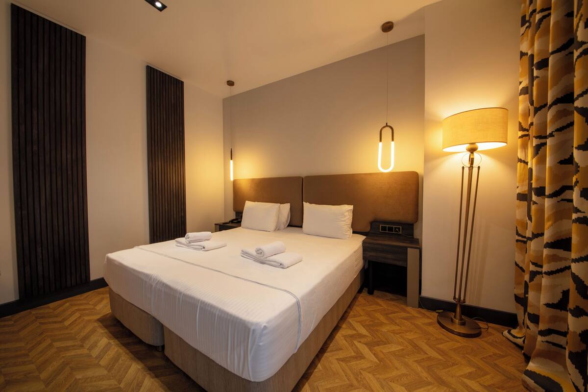 A hotel room with a large bed, a nightstand, a lamp, and a curtain.