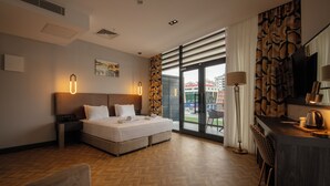 A hotel room with a bed, a desk with a lamp, a chair, and a view of the city through large windows. - V Center Hotel (Yomra)