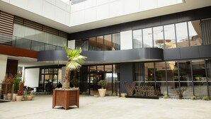 A modern hotel with a spacious atrium, large windows, and a central planter with a palm tree. - V Center Hotel (Yomra)