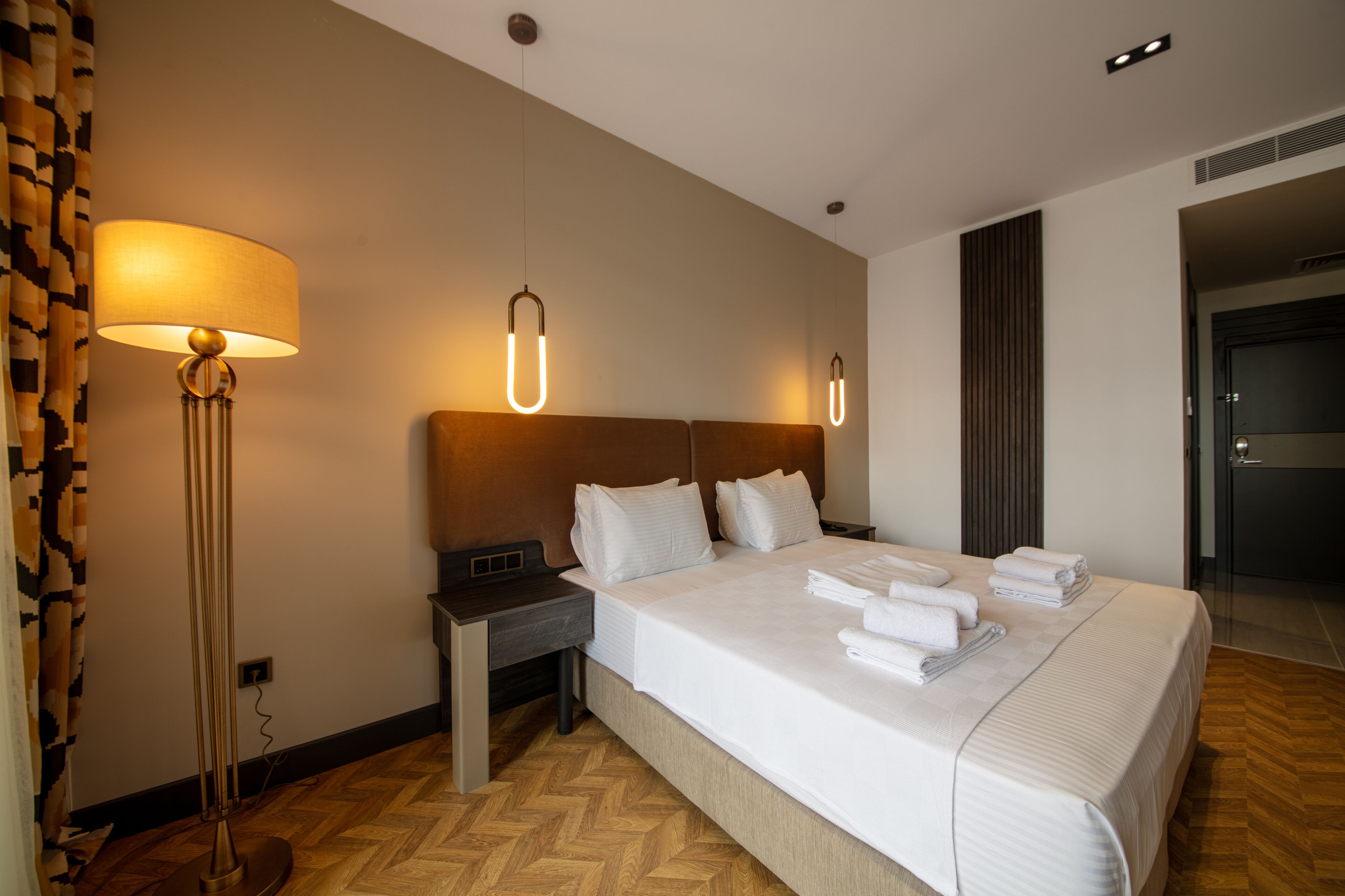 Una habitación de hotel con una cama grande, mesitas de noche, una lámpara de pie y un cabecero moderno.