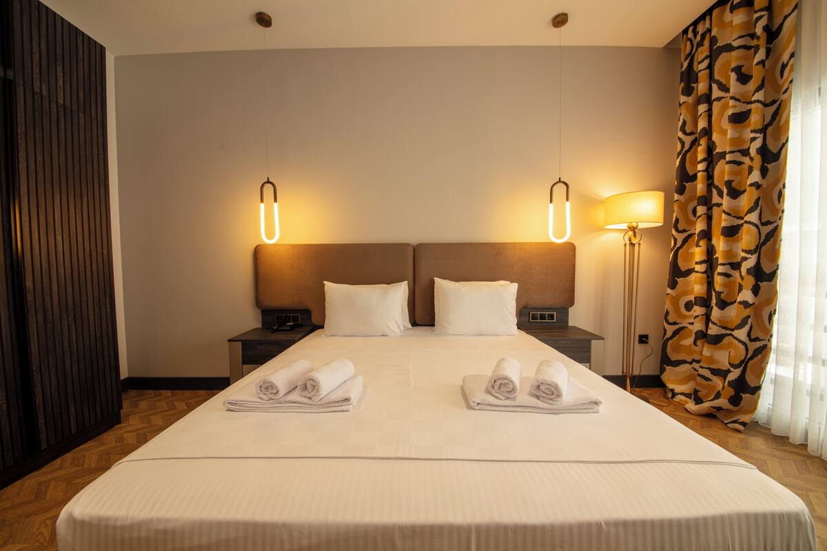 A hotel room with a large bed, two bedside tables, a lamp, and a curtain.