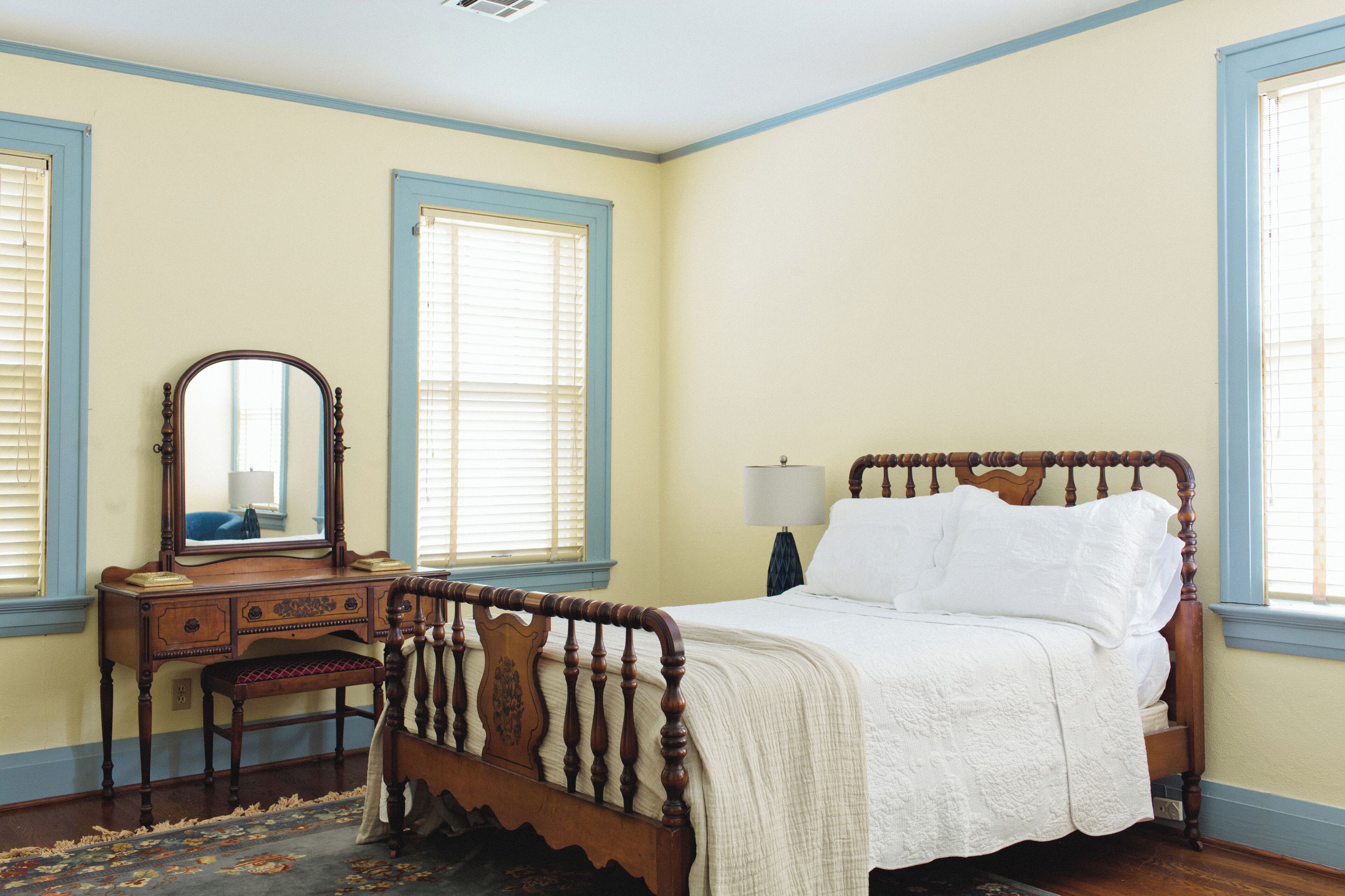 Un dormitorio con una cama de madera, una mesita de noche con lámpara, un aparador y un espejo.