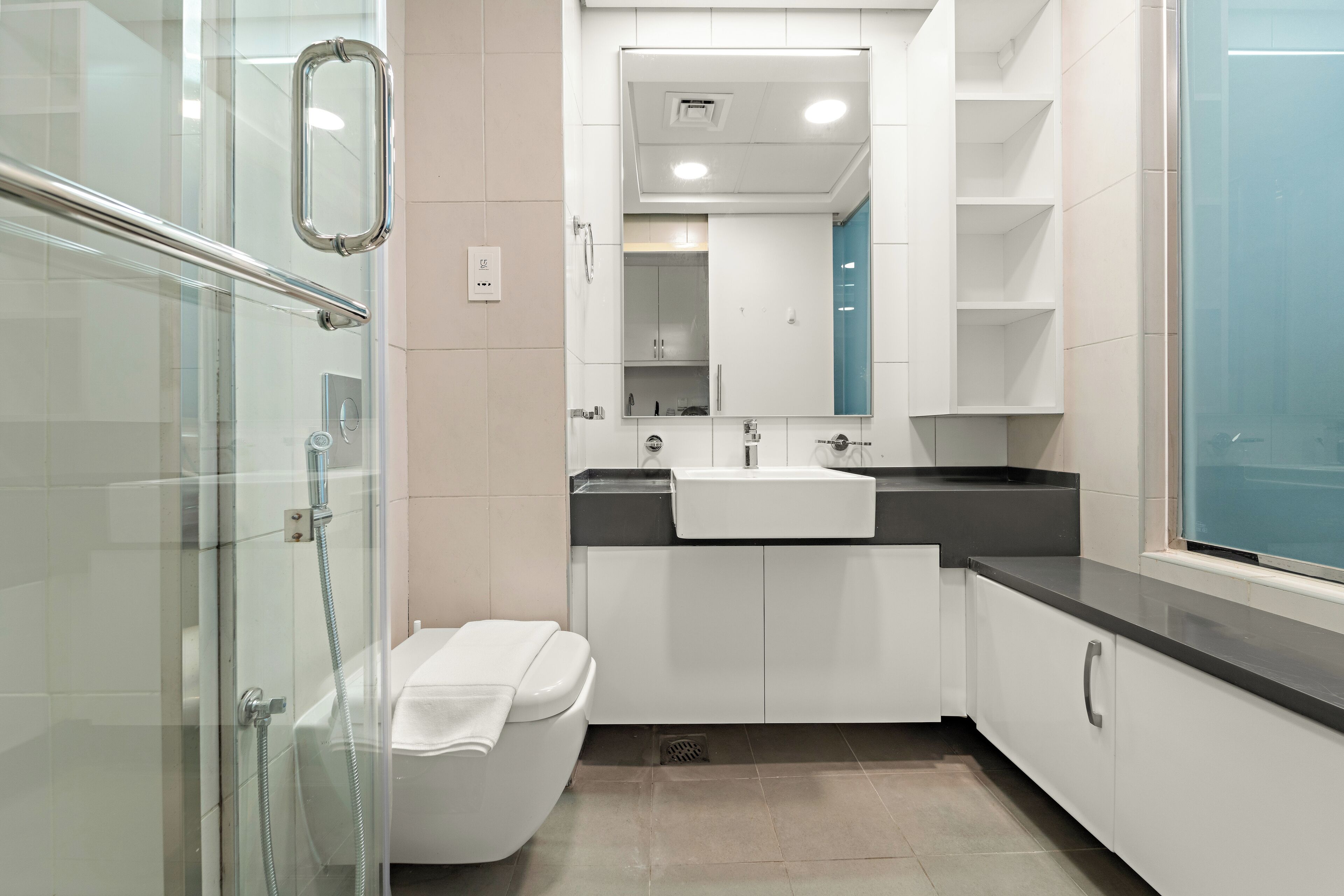 Een moderne badkamer met een glazen douchecabine, een wit toilet, een wastafel en een spiegel boven de wastafel.