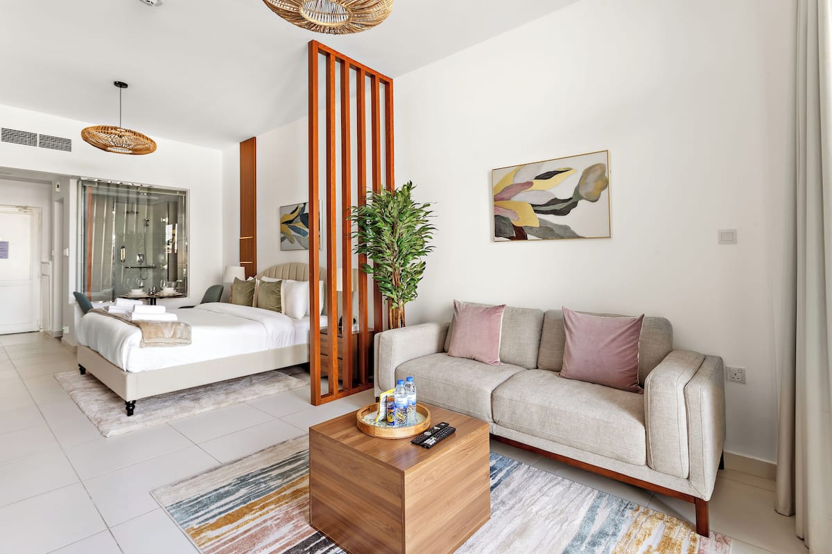 A modern hotel room with a bed, a sofa, a coffee table with a remote control, and a plant.