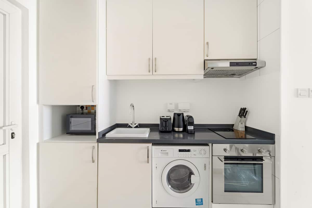 A compact kitchen with a washing machine, oven, and a coffee maker on the countertop.
