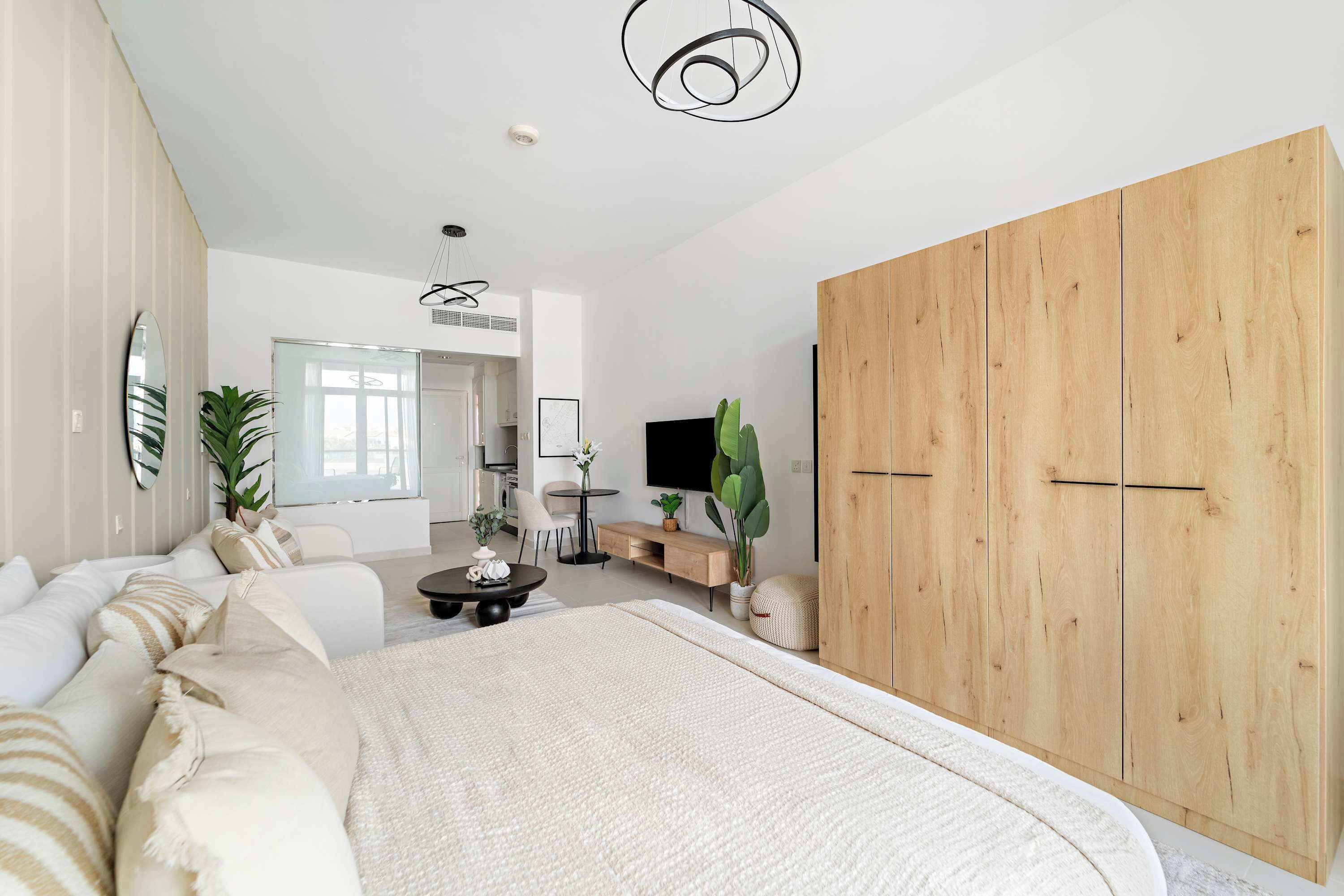 A modern bedroom with a large bed, a wooden wardrobe, a TV, and a dining area with a table and chairs.