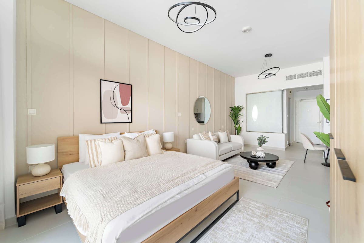 A modern bedroom with a large bed, bedside tables, a sofa, a coffee table, and a mirror.