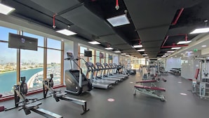 Une salle de sport équipée de tapis de course, d’appareils de musculation et offrant une vue sur le paysage urbain grâce à de grandes fenêtres.