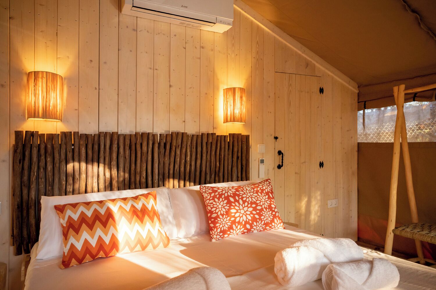 Quarto de madeira com uma cama, duas luminárias na parede e cabeceira de madeira.