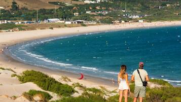 Vista costera con playa, dunas y algunos edificios al fondo.
