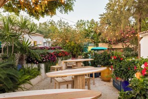 An outdoor patio area with wooden tables and benches, surrounded by lush greenery and flowering plants. - Dunas Tarifa (Tarifa)