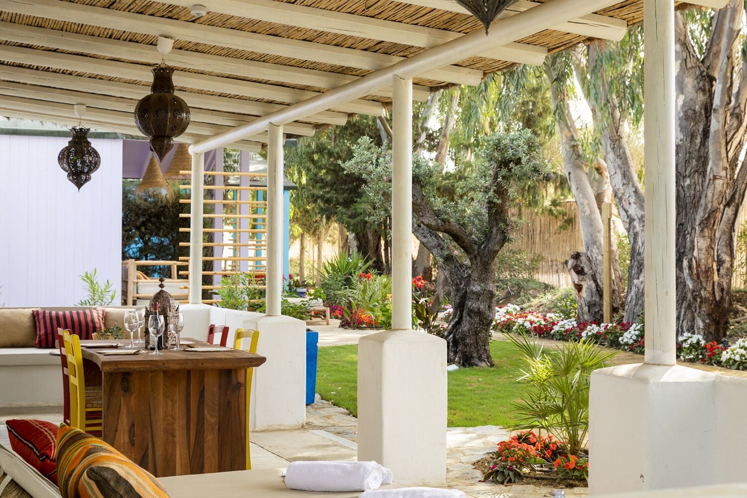 A covered outdoor seating area with a wooden table, chairs, and hanging lanterns.
