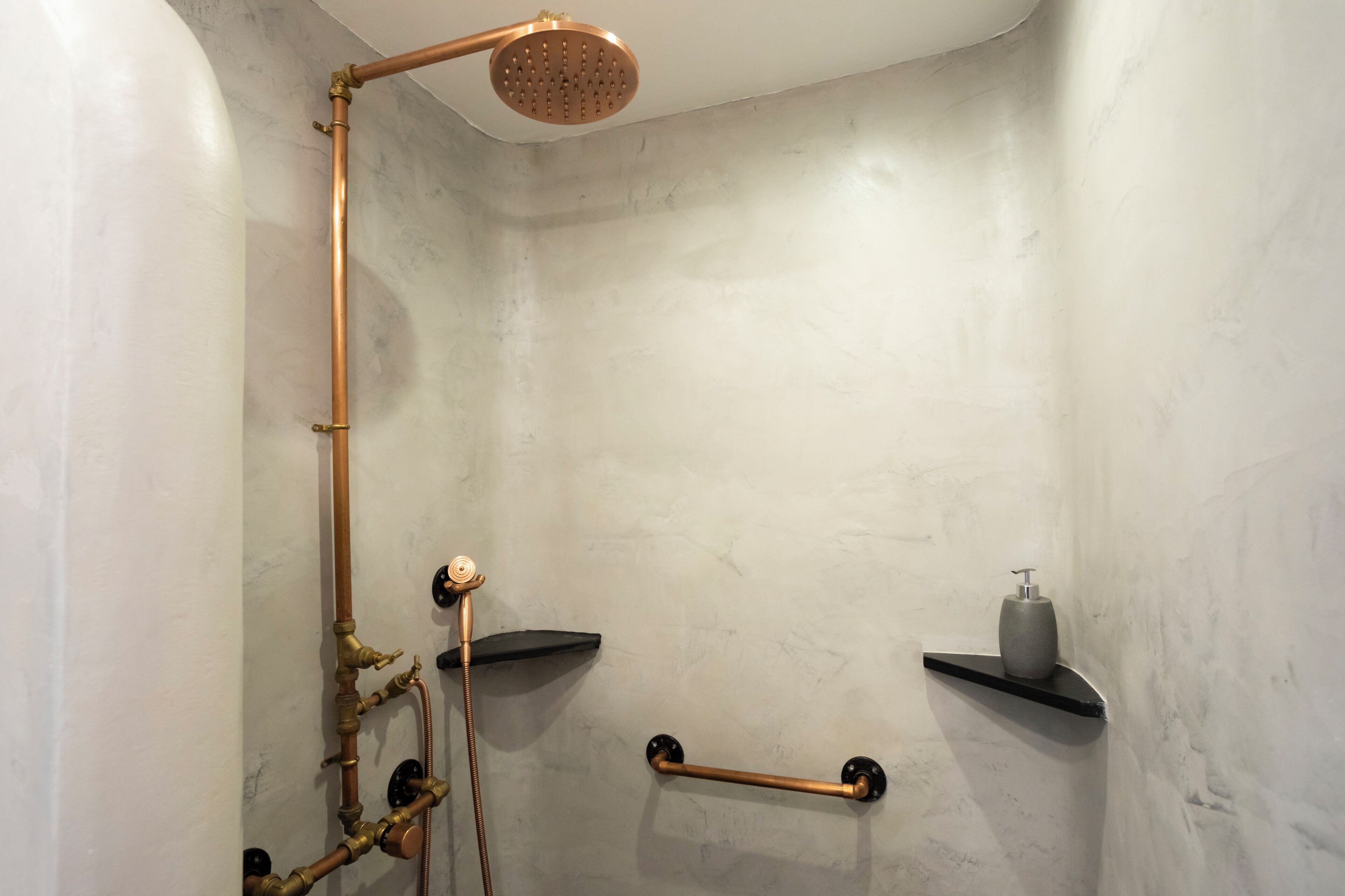 A modern shower with copper pipes, a handheld showerhead, and two black towel bars.