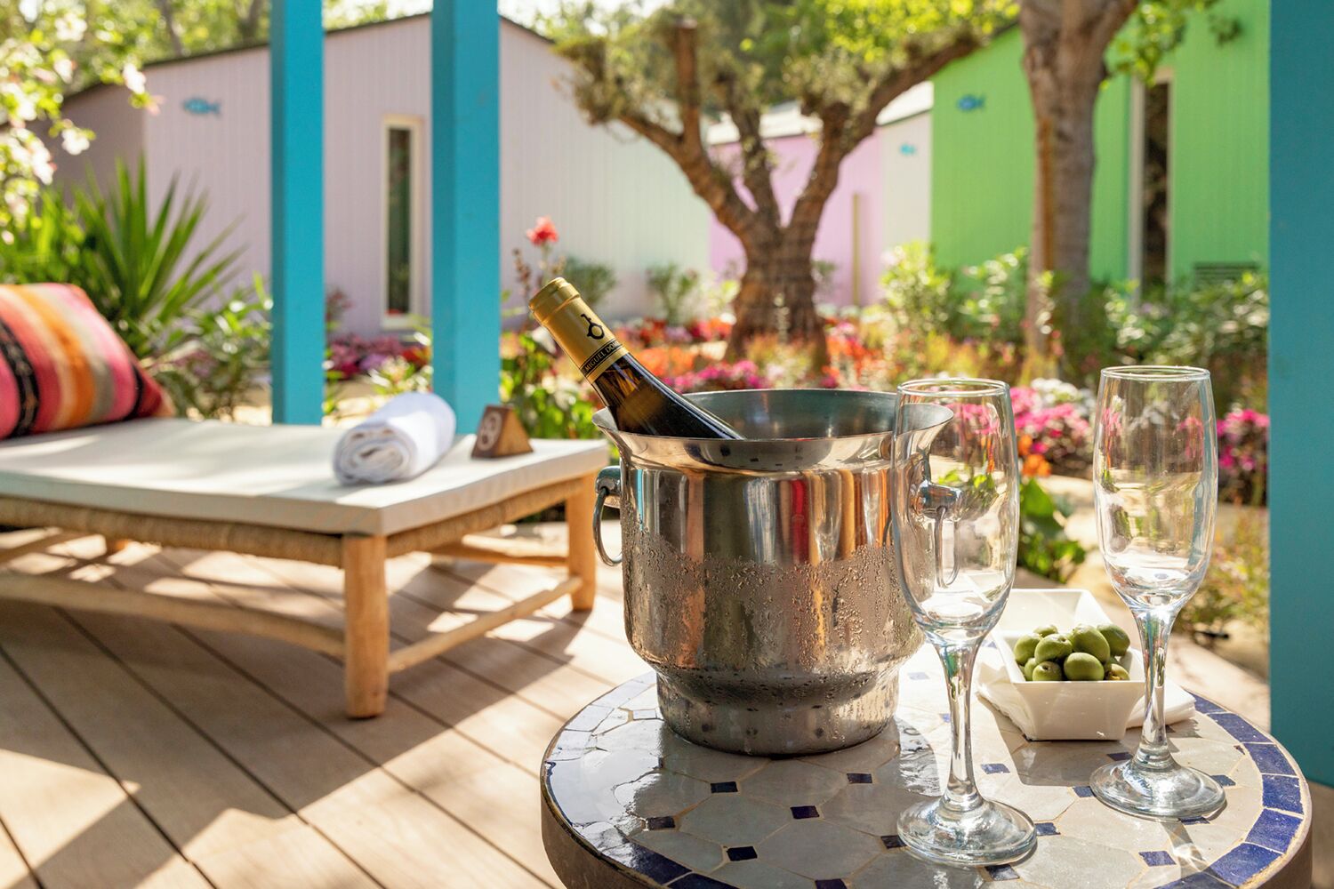A patio with a metal bucket containing a bottle, two glasses, and a bowl of olives.