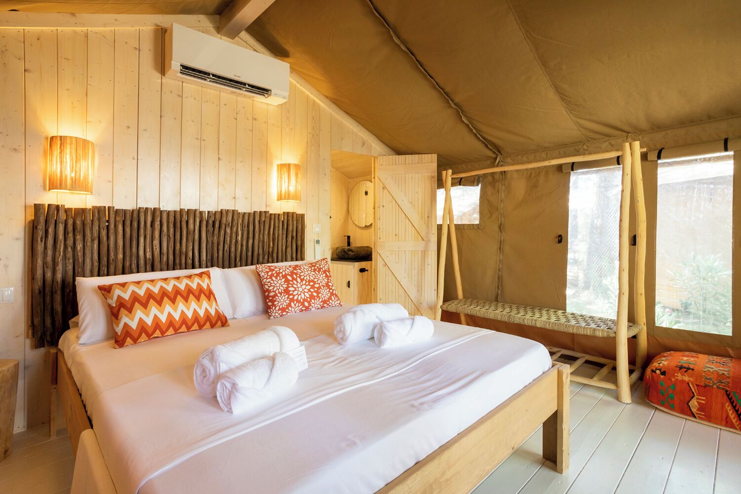 A cozy bedroom with a wooden bed, two wall-mounted lamps, and a window with a view of greenery.