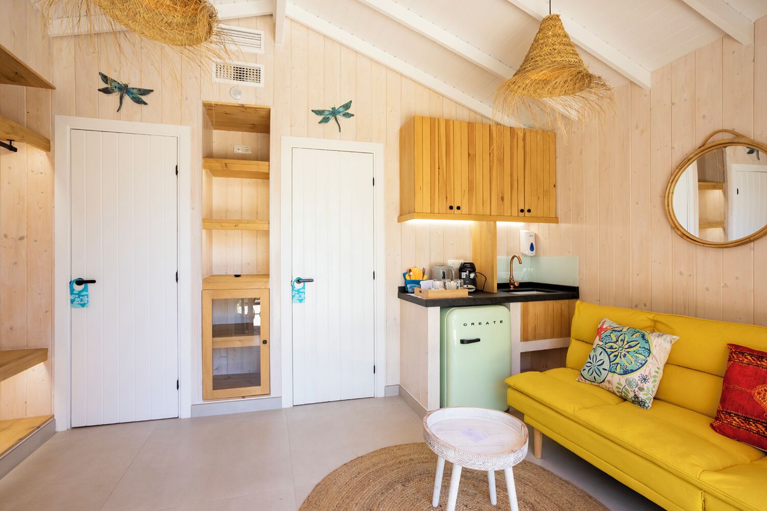 A cozy room with a yellow sofa, a small kitchen area, and a white door with a blue sign.