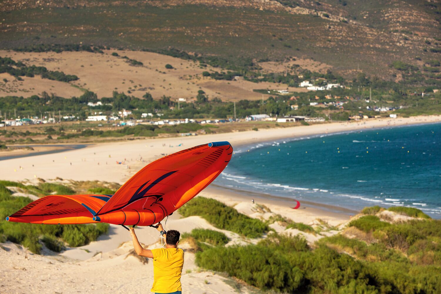 A beach with a person holding a large red kite.