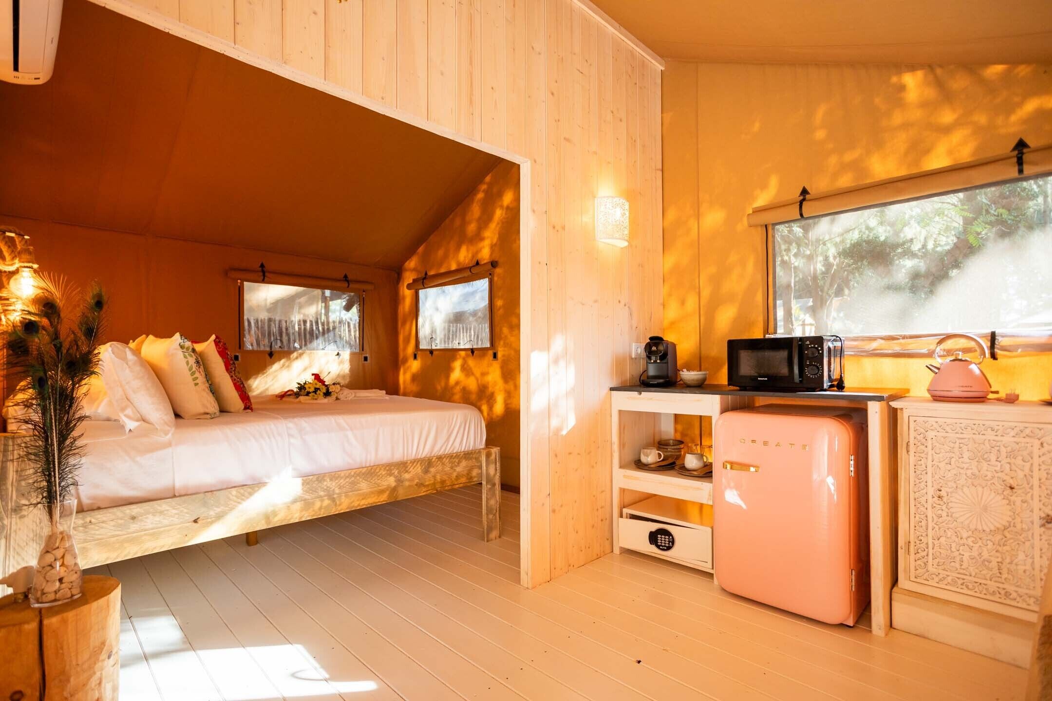 A cozy cabin with a bed, a kitchenette, and a window overlooking the forest.