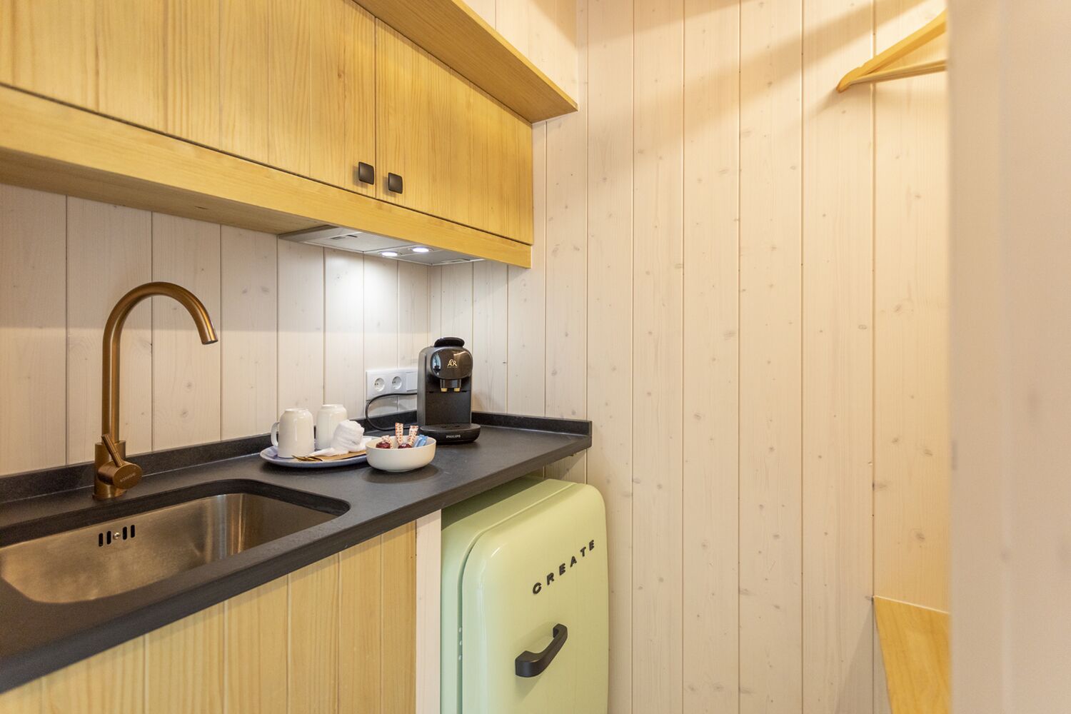 Ett modernt kök med träskåp, en diskho i rostfritt stål, en kaffemaskin och ett litet kylskåp.