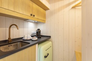 A modern kitchen with wooden cabinets, a stainless steel sink, a coffee machine, and a mini fridge.