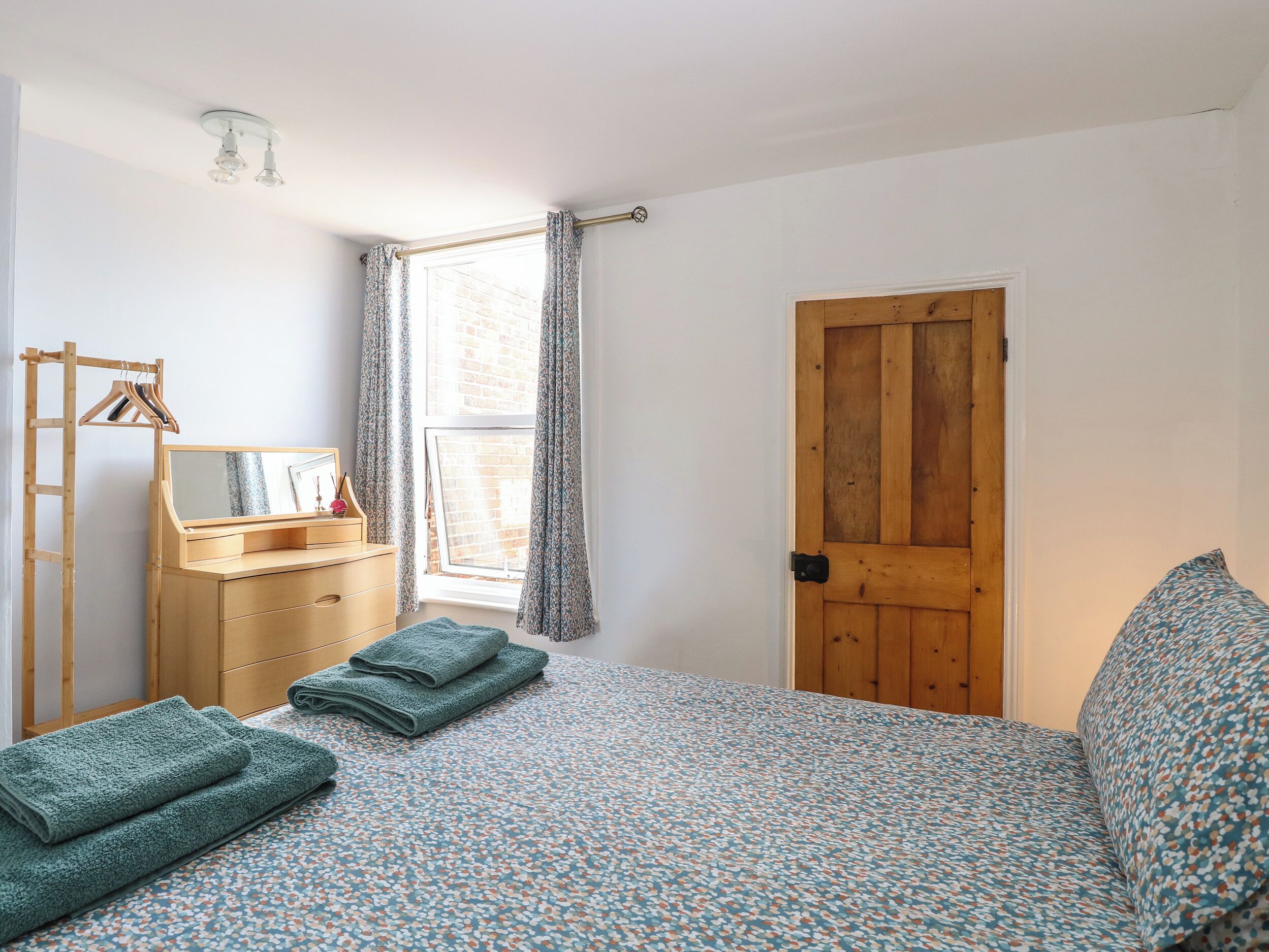 Une chambre à coucher avec un lit en bois, une commode en bois, un miroir et une fenêtre avec des rideaux.