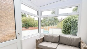 A sunroom with a wicker sofa, large windows, and a view of a garden. - Sole Bay Cottage (Lowestoft)