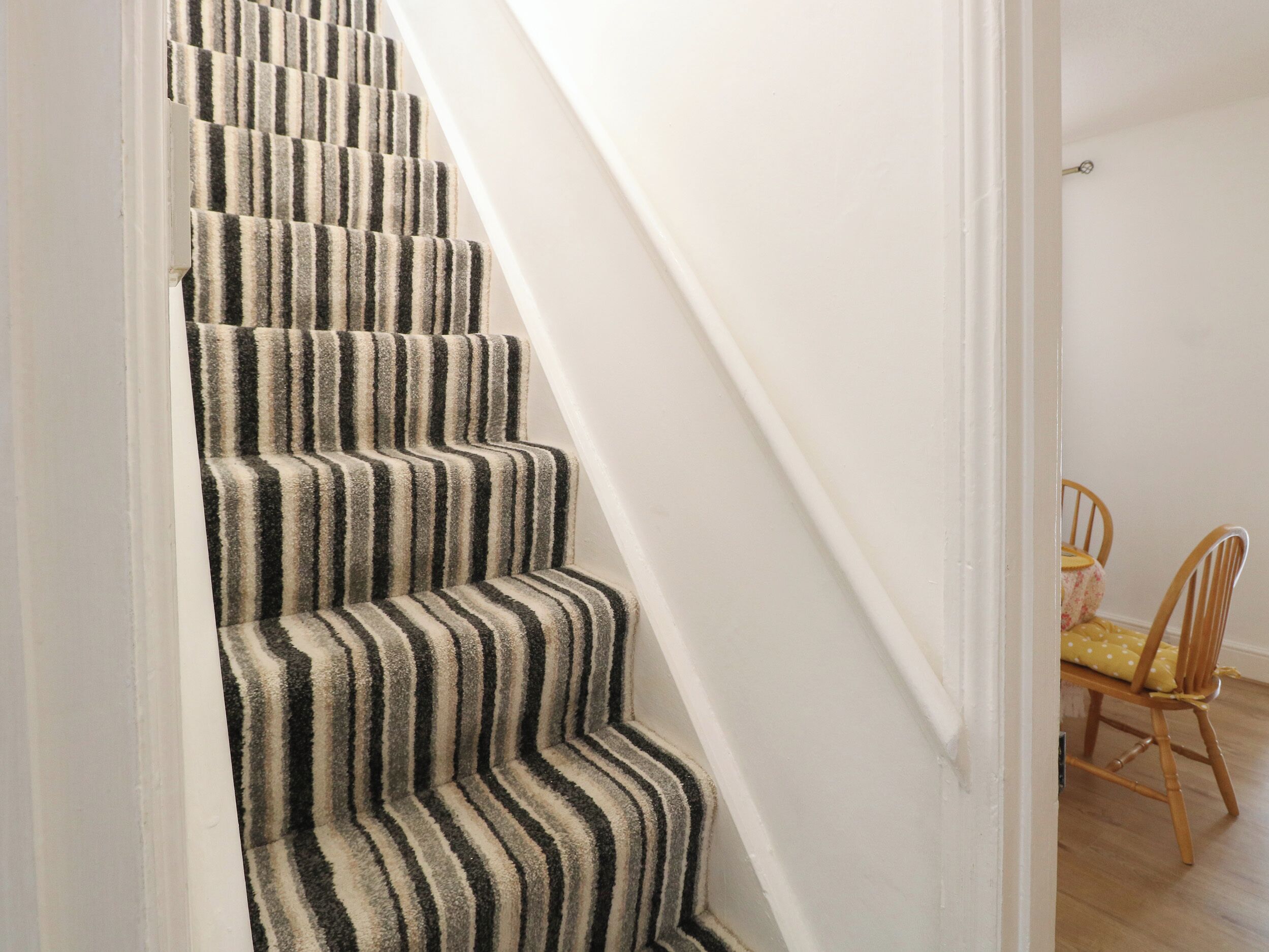 Un escalier recouvert d’une moquette à rayures et, au fond, une chaise en bois.