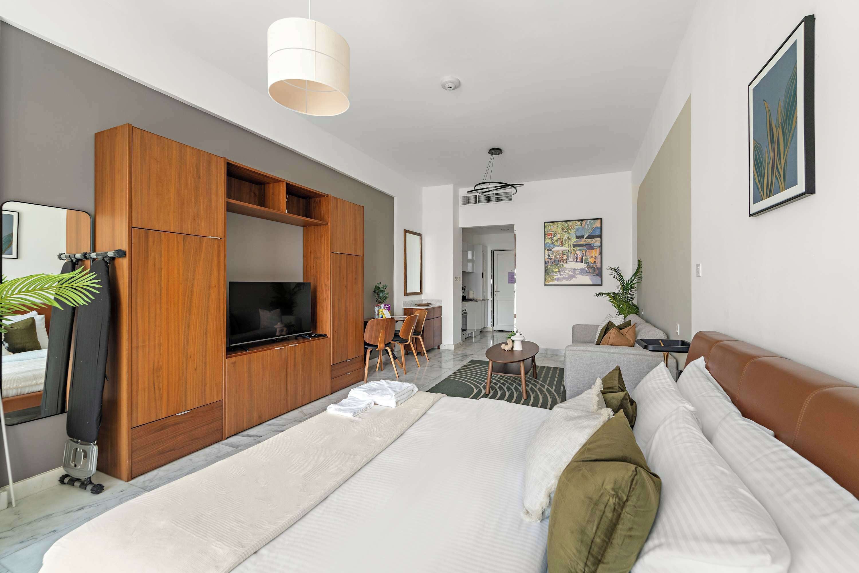 Quarto de hotel moderno com cama grande, guarda-roupa de madeira, televisão de tela plana e área de refeições com mesa e cadeiras.