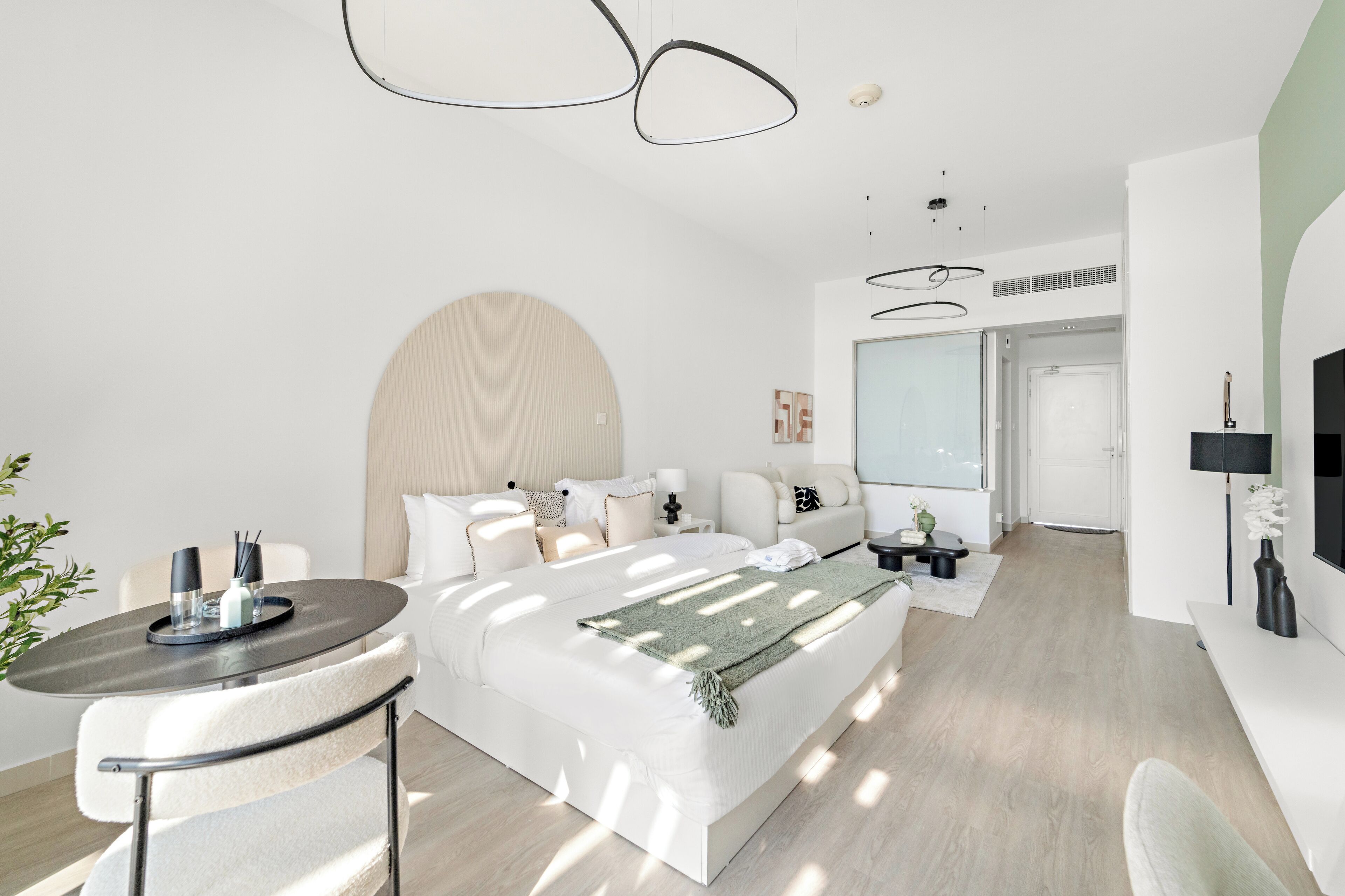 A modern hotel room with a large bed, a small table with a tray, a sofa, and a TV.