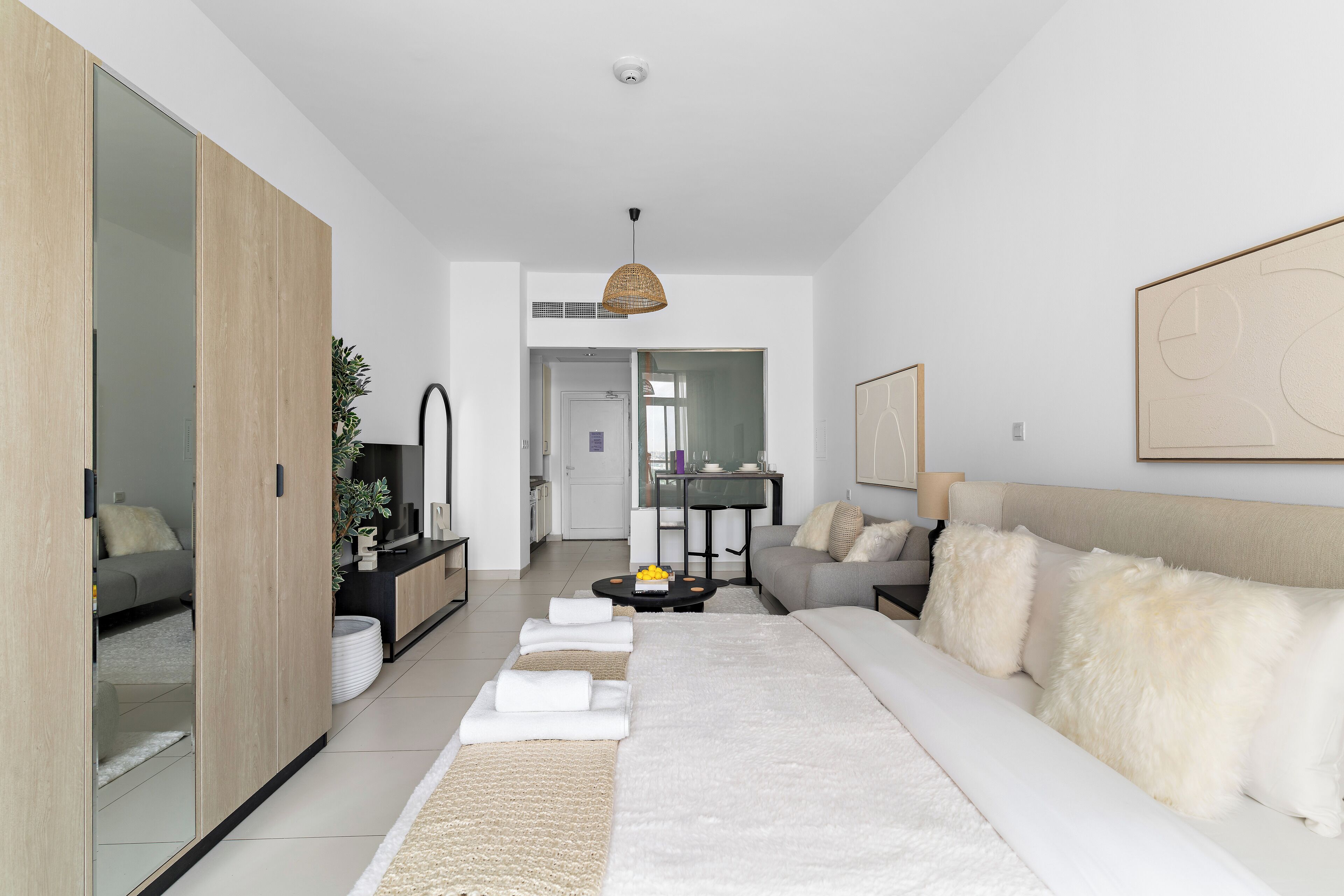 A modern hotel room with a large bed, a sofa, a dining area, and a sliding door closet.