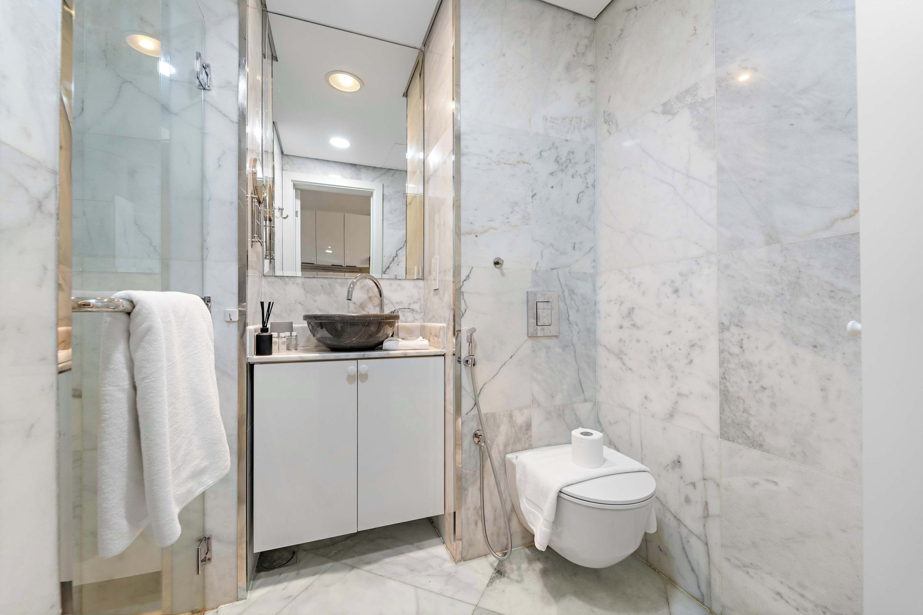Une salle de bain moderne avec une douche à parois de verre, des toilettes blanches et un pare-baignoire en marbre.