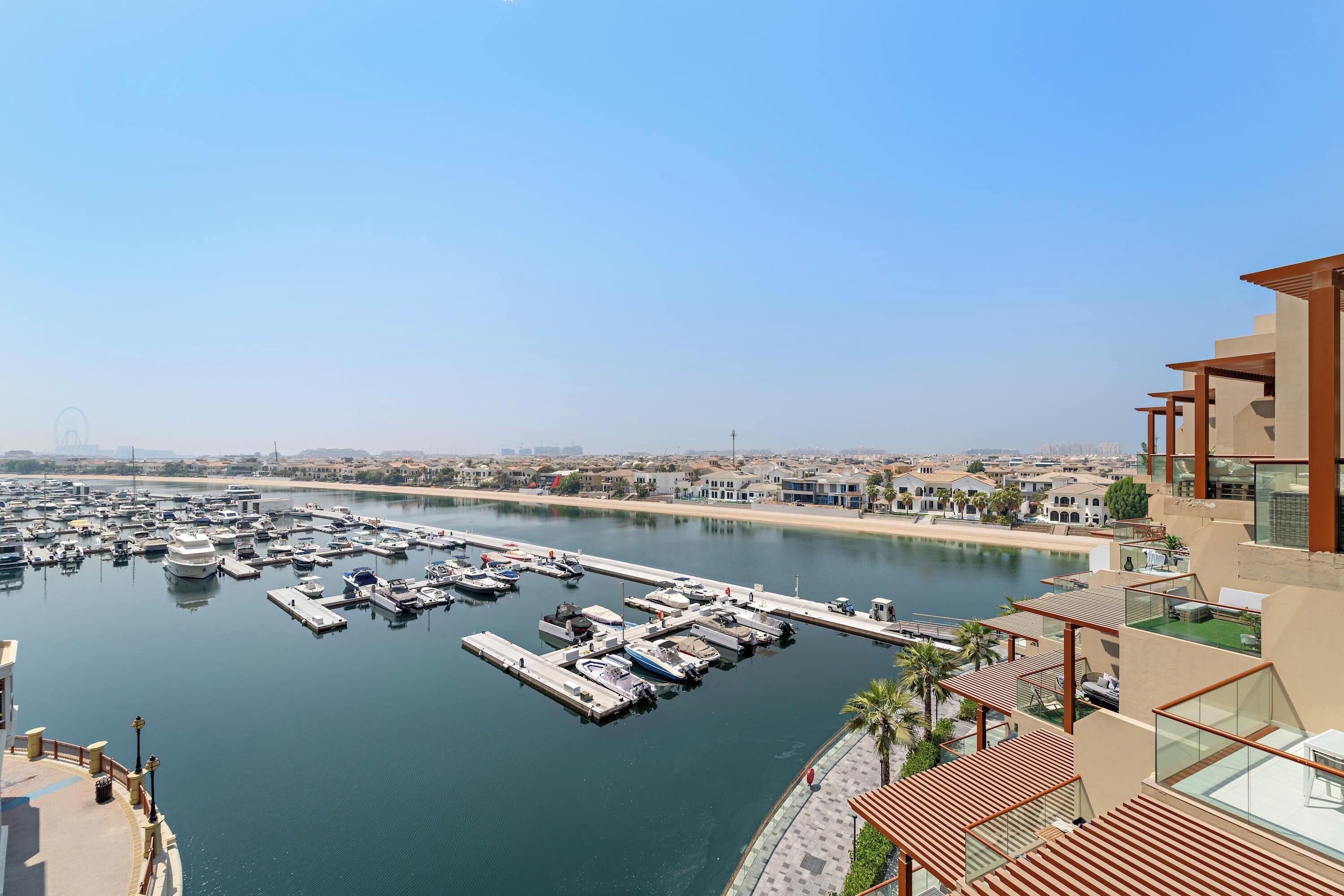 A marina with numerous boats docked, a clear sky, and a modern building with a rooftop terrace.