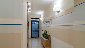 Un couloir avec un comptoir d’accueil, une plante en pot et une enseigne indiquant « Col Margherite, chambre d’hôtes ».