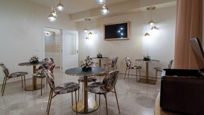 Un espace repas avec des tables rondes et des chaises à motifs, un téléviseur à écran plat fixé au mur et des luminaires suspendus.