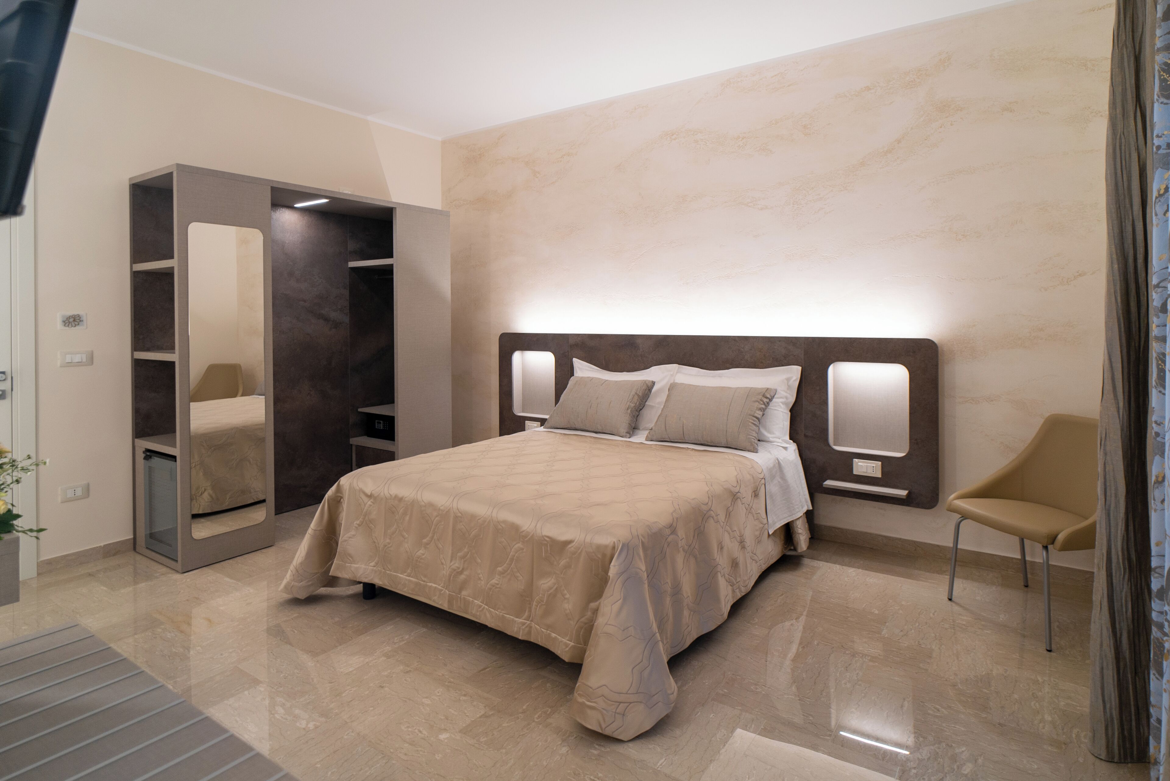 A modern bedroom with a large bed, a built-in wardrobe, and a seating area.