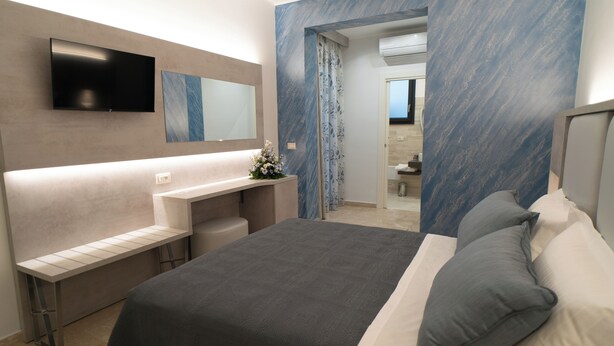 Une chambre à coucher moderne, avec un lit, des tables de chevet, un téléviseur et une salle de bain visible à travers une porte ouverte.