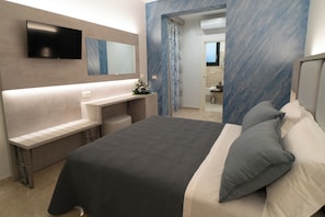 Un dormitorio moderno con cama, mesitas de noche, televisor y baño visible a través de una puerta abierta.