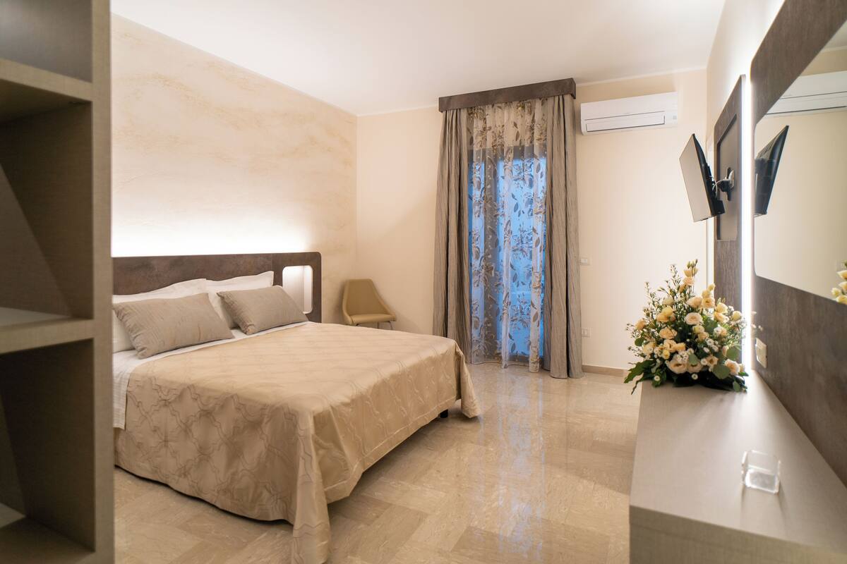 Un dormitorio con una cama, una silla, un escritorio y una ventana con cortinas.