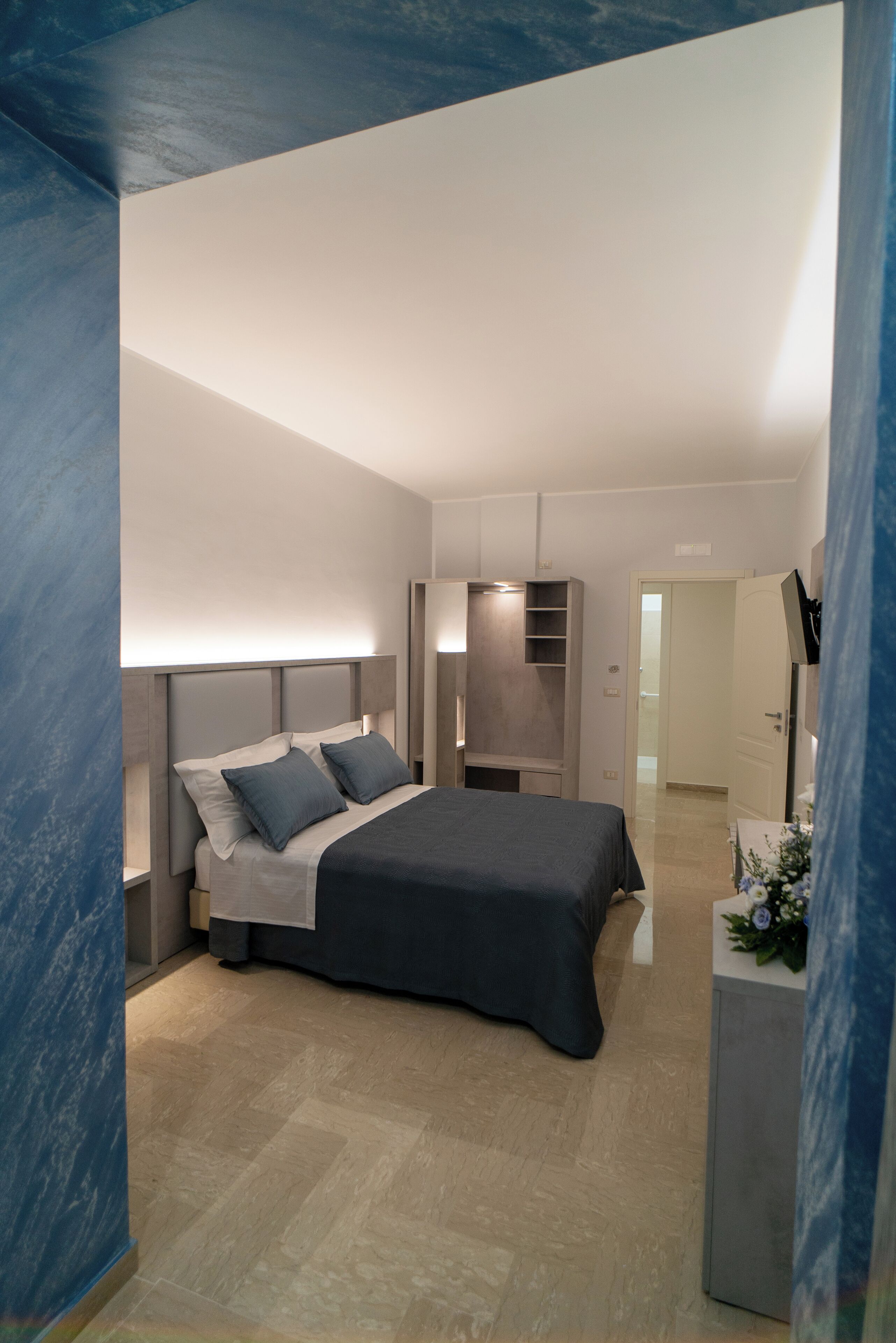 Quarto moderno com cama, mesas de cabeceira, guarda-roupa e escrivaninha com planta.
