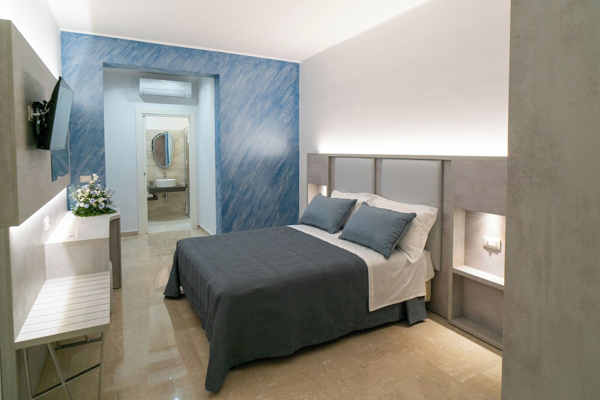 Un dormitorio moderno con cama, mesita de noche y televisor montado en la pared.